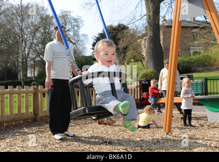 Baby Junge auf Schaukel im Spiel Bereich Kinderspielplatz in Telford, Großbritannien Stockfoto