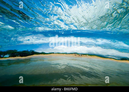 Unterwasser Blick durch eine klare Welle in Richtung Strand, mit Menschen zu Fuß am Strand. Stockfoto