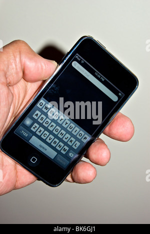 Hand mit Apple iPod Touch mit Fingerabdruck verschmiert Touch Bildschirm Schreibmaschine QWERTZ-Tastatur Stockfoto