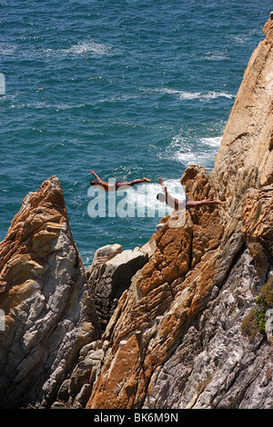 Zwei Taucher tun "Swan Dive" aus der berühmten Klippen von La Quebrada in den stürmischen Ozean und Bucht von Acapulco, Mexiko Stockfoto