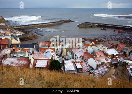 Winterwetter & schneebedeckte Dächer. Die schneebedeckten roten Ziegeldächer der Fischerhäuser am Meer in Staithes, North Yorkshire National Park, Großbritannien Stockfoto