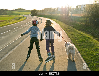 2 Kinder auf Inlineskates Haustier Hund spazieren gehen. Stockfoto