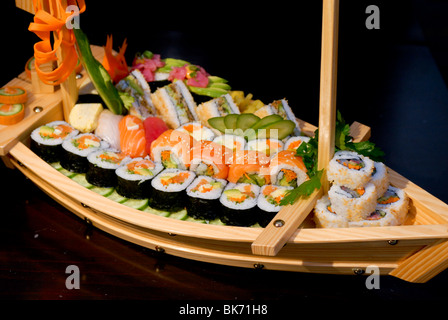 Auswahl an Sushi auf einem Holzboot geformte Platte einschließlich: Sushi Maki, Futo Maki Insideout und Sushi-Sandwich Stockfoto