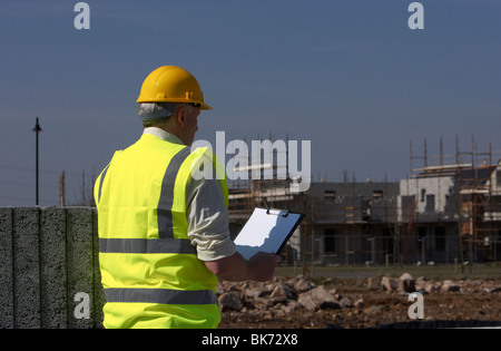 Mann mittleren Alters grauen Haaren tragen Schutzhelm und Flexarbeiten Weste mit einem Klemmbrett Bausteine auf Bau Baustelle Stockfoto