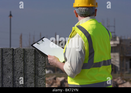 Mann mittleren Alters grauen Haaren tragen Schutzhelm und Flexarbeiten Weste mit einem Klemmbrett Bausteine auf Bau Baustelle Stockfoto