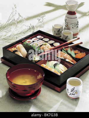 Japanisches Sushi Box mit Suppe und Saki, Stäbchen auf einen hellgrünen Hintergrund mit Schlagschatten. Stockfoto