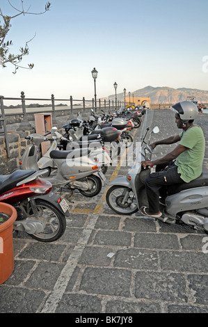 Ein italienischer Mann parkt ein moped im vespa-Stil in der Hafenstadt Santa Marina, auf der Äolischen Insel Salina, Sizilien, Italien. Stockfoto