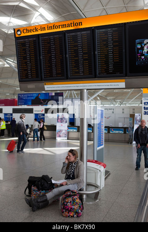 Ein Passagier sitzt unten ein Flughafen Check-in Informationen Board zeigt alle Flüge abgesagt sprechen in ihrem Mobiltelefon Stockfoto