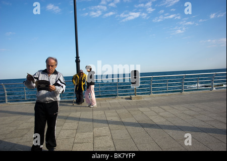 Ein Bewohner von Beirut lesen Magazin auf dem Gesims des Beirut Libanon während der andere mit der gelben Jacke betteln Stockfoto