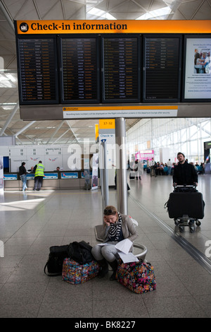 Ein Passagier sitzt unten ein Flughafen Check-in Informationen Board zeigt alle Flüge abgesagt sprechen in ihrem Mobiltelefon Stockfoto