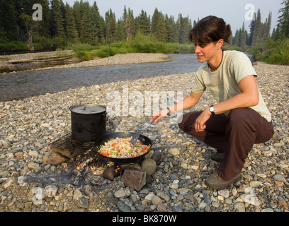 Junge Frau, Kochen, Braten Huhn rühren braten am Lagerfeuer, Kiesbank, oben Liard River, Yukon Territorium, Kanada Stockfoto