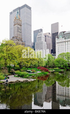 NEW YORK, NY, Vereinigte Staaten – der Teich im New Yorker Central Park spiegelt die lebhaften Farben des Frühlings wider, mit blühenden Bäumen und frischem Laub rund um das ruhige Wasser. Im Hintergrund erhebt sich die berühmte Skyline von Manhattan über dem Park und schafft einen eindrucksvollen Kontrast zwischen der natürlichen Oase und der urbanen Landschaft von Midtown. Stockfoto