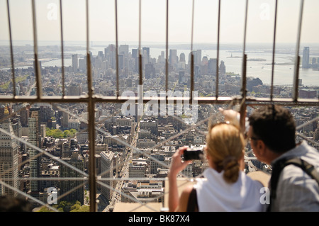 Empire State Building Observation Deck View New York City // NEW YORK, New York — Tourists admire the view from the top of the Empire State Building in New York City on a clear spring day. The observation deck offers stunning panoramic views of Manhattan and beyond, making it one of the most iconic tourist attractions in the city. Stockfoto