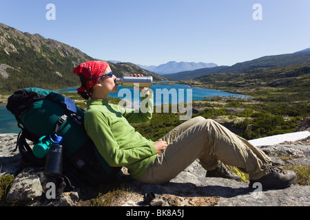 Junge Frau, Wanderer, Backpacker, sitzt auf einem Felsen, trinken, ruhen, genießen Panorama, Deep Lake, historische Chilkoot Pass, Chi Stockfoto