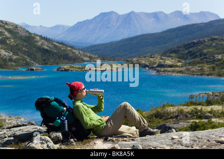 Junge Frau, Wanderer, Backpacker, sitzt auf einem Felsen, trinken, ruhen, genießen Panorama, Deep Lake, historische Chilkoot Pass, Chi Stockfoto