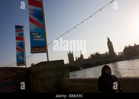 Eine muslimische Frau touristische Spaziergänge entlang der Böschung hinter Parlament unter konservativen Wahl Banner. Stockfoto