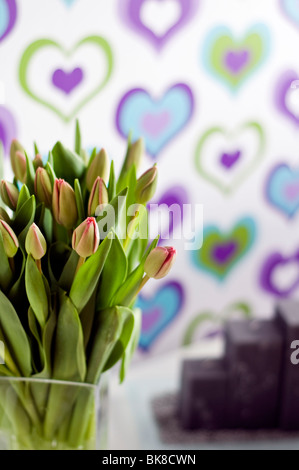 Eine Vase mit violette Tulpen vor bunten Tapete verziert mit einem Herz-Muster Stockfoto