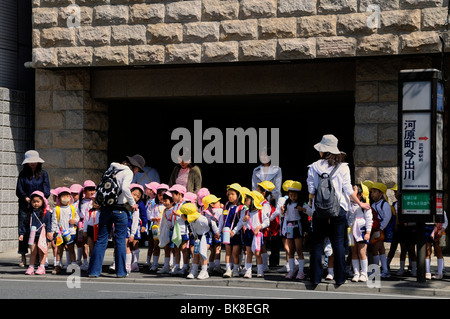 Kinder, Mädchen mit gelben und Jungen mit rosa Mützen, warten in der Innenstadt für den Bus, Kyoto, Japan, Asien Stockfoto