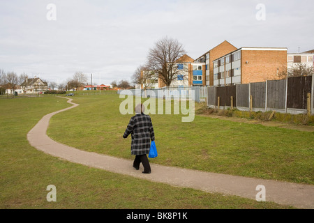 Eine Frau geht einen Weg durch einen Park neben einer Wohnsiedlung. Stockfoto