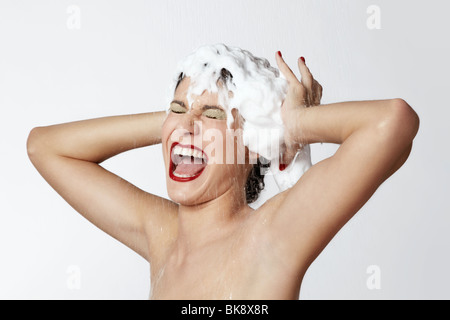Fröhliche junge Frau in der Dusche mit Schaum im Haar Stockfoto