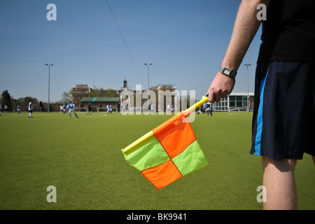 Eine Nahaufnahme von einem Linienrichter Midrift bei einem Amateur Fußball- oder Fußball-Match in London. Auch ist eine gelbe und orange Flagge. Stockfoto
