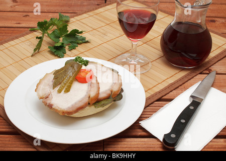 Schwein braten Sandwich mit Gurke Ventilator und geschnittenen Kirschtomaten, Karaffe und Glas Rotwein gerollt, Messer Stockfoto