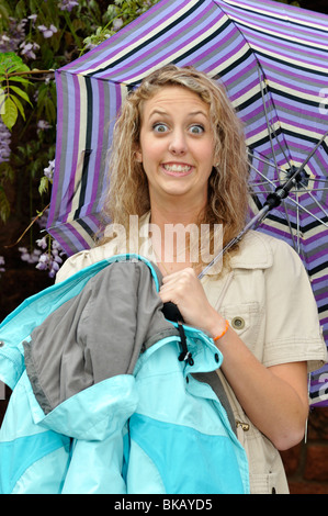 Ein kaukasischer Jugendmädchen hält einen Schirm und Mantel und macht ein lustiges Gesicht. USA. Stockfoto