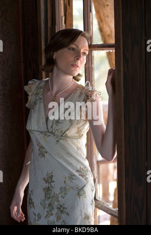 Eine schöne junge kaukasischen Frau steht in der Nähe einer Wand in ein altes verlassenes Haus, beim Blick aus dem Fenster gelehnt. Stockfoto