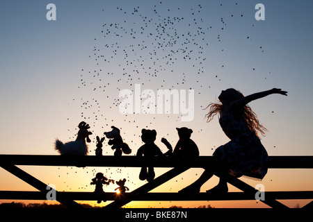 Mädchen Wurfsterne über eine Stoffpuppe, Huhn, Fuchs, Hase, Katze und Teddy Bear Stofftiere sitzen auf ein Tor bei Sonnenuntergang. Silhouette Stockfoto