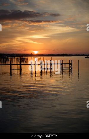 Stuten Schwänzen Wolken in einem tief orange Sonnenuntergang mit Pfählen im Wasser. Stockfoto