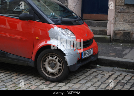 Smart Auto geparkt auf einer gepflasterten Straße mit einigen Schaden vorübergehend mit silbernen Klebeband repariert. Stockfoto