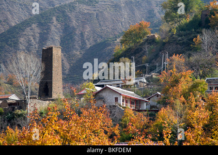 Obstgarten mit roten Herbst Blätter in Farm, die eine alte historische Wehrturm in der Regel in tibetischen Gebieten Qiang, China gefunden hat. Stockfoto