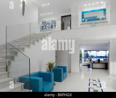 Blaue Sessel und weiß geflieste Fußböden in großen modernen weißen Saal mit Glas Geländer auf Treppe Stockfoto