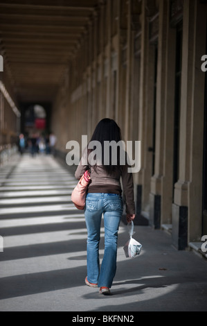 Menschen, die Urban Park, Jardin du Palais Royale, French Gardens, Spring, Paris, Frankreich, Düstere Frau, die in der Kolonnade des pariser palais royale mit Taschen davonläuft Stockfoto