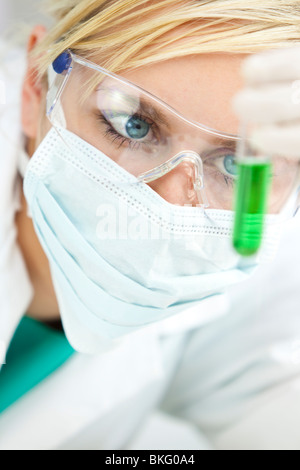 Eine blonde medizinische oder wissenschaftliche Forscher oder Arzt Blick auf ein Reagenzglas grüne Flüssigkeit in einem Labor Stockfoto