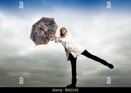 blonde Frau hält sich an einen Regenschirm im wind Stockfoto