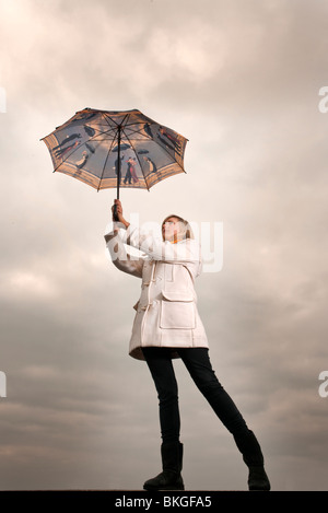 blonde Frau hält sich an einen Regenschirm im wind Stockfoto