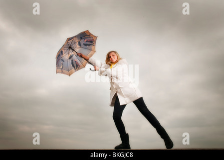 blonde Frau hält sich an einen Regenschirm im wind Stockfoto