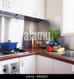 Holz Arbeitsplatten auf montierten Einheiten in moderne weiße Küche mit Edelstahl-Splash-Rücken und blauen Pfanne auf dem Kochfeld Stockfoto
