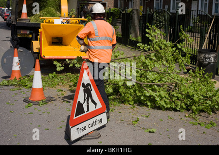 In der Nähe ein Mann am Werk-Warnschild füttern Rates Baum Chirurgen frisch geschnittenen Zweige in einen Schredder, da eine Straße aus coned ist. Stockfoto