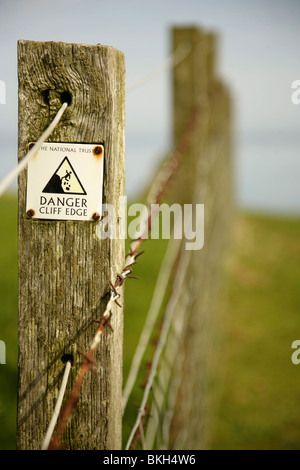 Gefahr Cliff Edge Warnschild am Stacheldraht-Zaun in der Nähe von Dunstanburgh Castle, Northumberland, Vereinigtes Königreich. Stockfoto