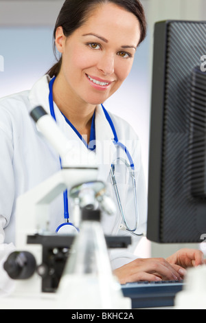 Eine lächelnde medizinische oder wissenschaftliche Forscher oder Frau Ärztin mit einem Computer in einem Labor mit Mikroskop Stockfoto