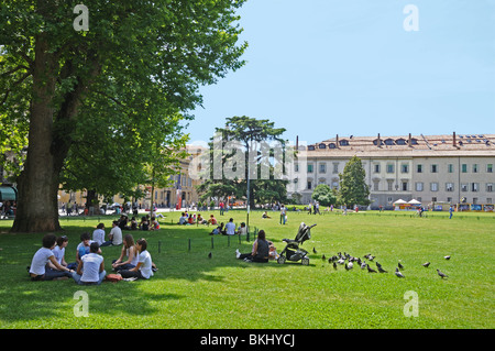 Junge Leute und Studenten unter Bäumen auf grünen Rasenflächen im öffentlichen Park Piazza della Pace-Parma-Italien Stockfoto