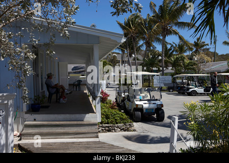 Ein Mann sitzt auf der Veranda in einer tropischen Umgebung mit Golf-Carts geparkt vor der Tür. der Mann O Krieg Marina auf Mann O Krieg Cay. Stockfoto