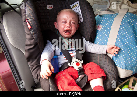 Baby Junge (1 Jahr alt) in einem Autositz für mehr Schokolade mit einem schmutzigen Mund schreien. Stockfoto