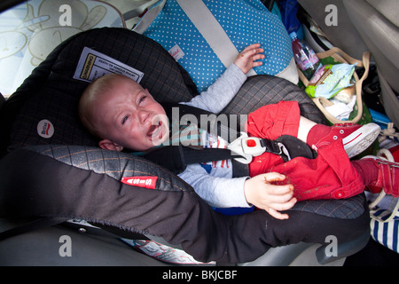 Baby Junge (1 Jahr alt) in einem Autositz für mehr Schokolade mit einem schmutzigen Mund schreien. Stockfoto