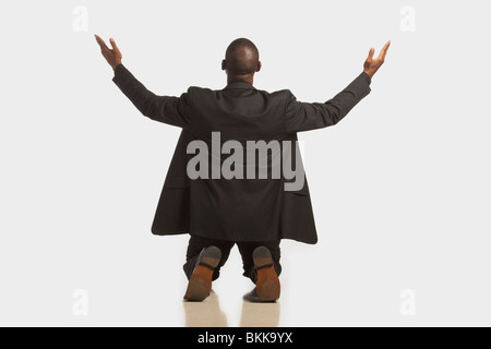 Ein Unternehmer trägt einen schwarzen Anzug, kniete mit erhobenen Händen Stockfoto
