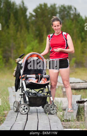 Junge Mutter mit Kinderwagen und ein Baby drin. Sie steht auf einem hölzernen Laufsteg, der durch den Sumpf lief. Die Wälder von Karelien Stockfoto