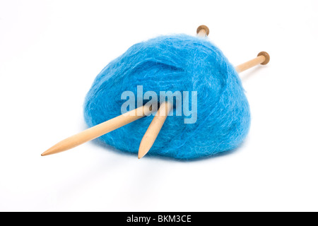 Eine große Kugel aus blaue Mohairwolle durchbohrt mit großen hölzernen Stricknadeln gegen weiß. Stockfoto