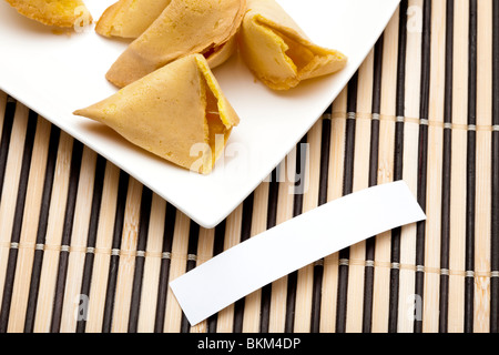 Fortune Cookies auf einem Teller, einem Cookie gebrochen, leere Messagetag auf Bambusmatte. Füllen Sie Ihre eigene Botschaft. Stockfoto